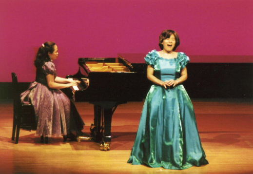 写真２　ステージ中央　金子眞理子（水色のドレス）　ピアノ　坂巻明子（ベージュのドレス）