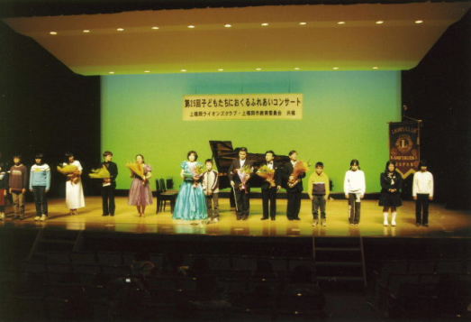 写真５　花束贈呈を受けた演奏者と、渡した小学生がステージ上に一列に並んでいる